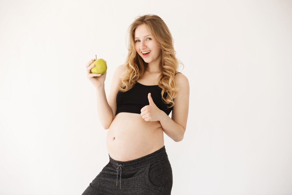 beautiful young mother with blond hair black clothes smiling holding apple near pregnant belly showing thumb up beautiful young mother with blond hair black clothes smiling holding apple near pregnant belly showing thumb up