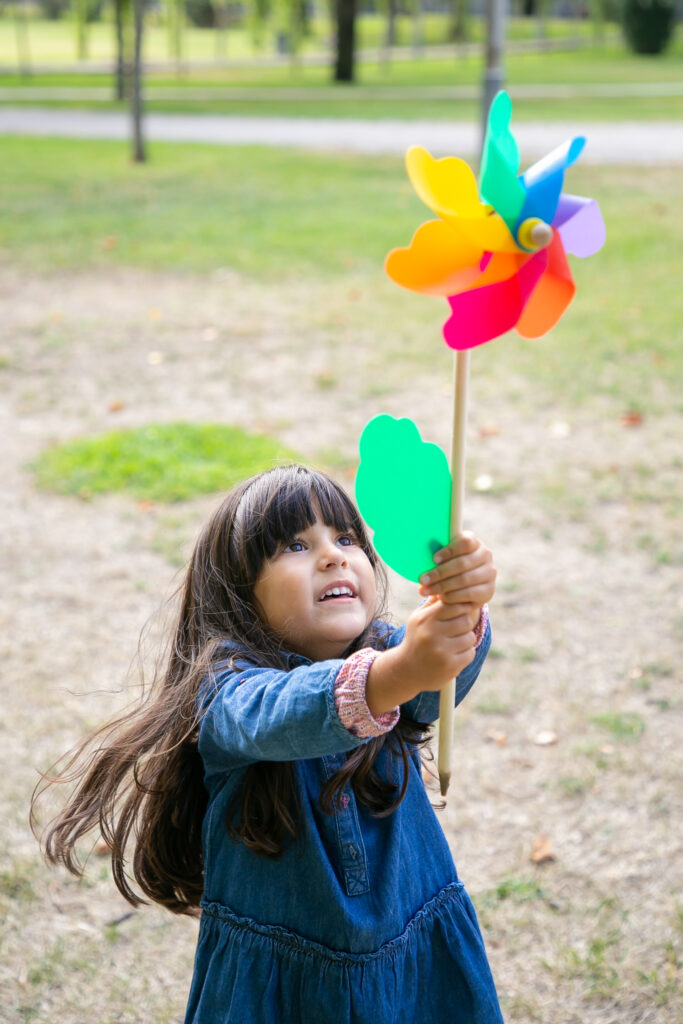 cheerful black haired girl playing park holding raising pinwheel looking toy excitement vertical shot children outdoor activity concept cheerful black haired girl playing park holding raising pinwheel looking toy excitement vertical shot children outdoor activity concept