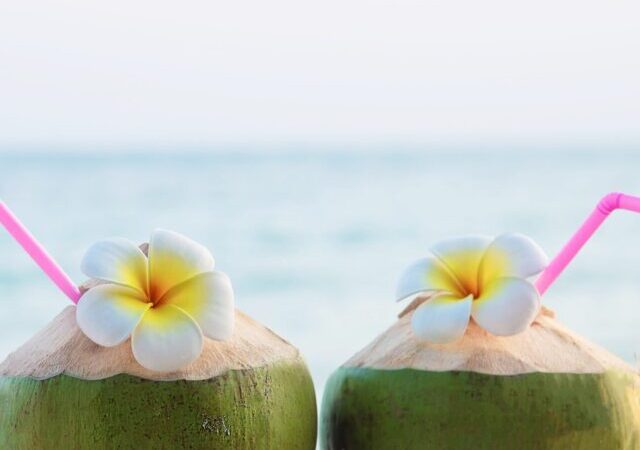 fresh-coconut-couple-hands-with-plumeria-decorated-beach-with-sea-wave-honeymoon-couple-tourist-with-fresh-fruit-sea-sand-sun-vacation-concept