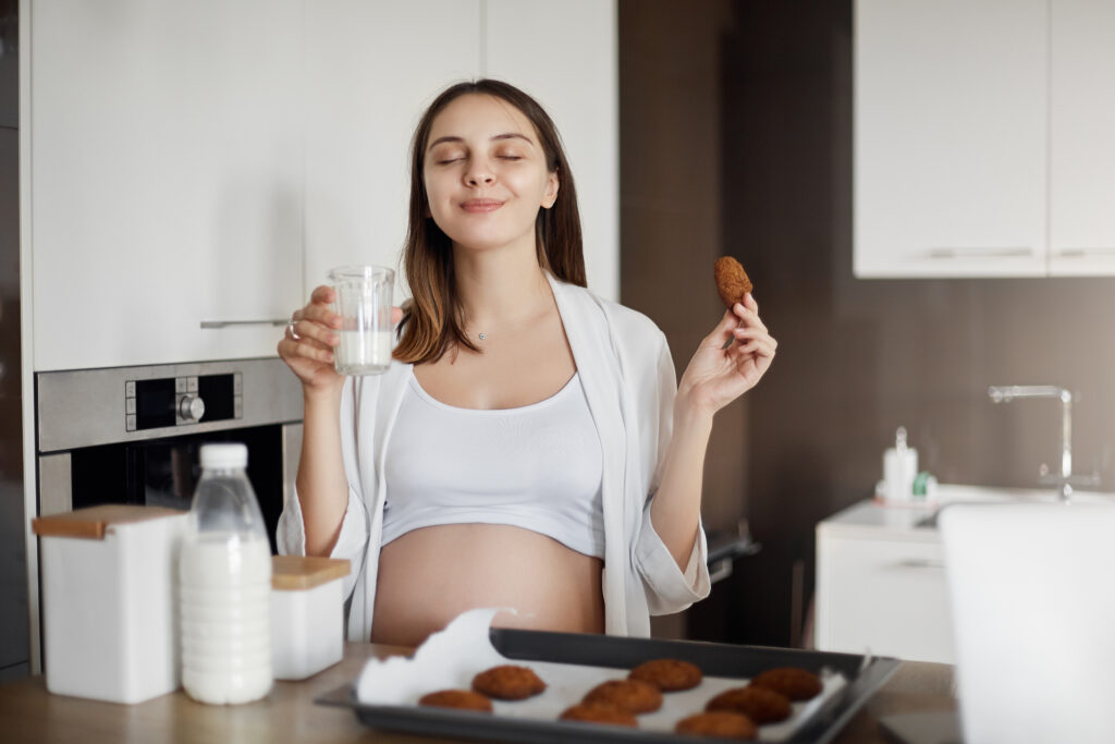 pregnant woman feeling delight joy enjoying great taste fresh baked cookies drinking warm milk closing eyes smiling holding glass cookie sitting near kitchen table pregnant woman feeling delight joy enjoying great taste fresh baked cookies drinking warm milk closing eyes smiling holding glass cookie sitting near kitchen table